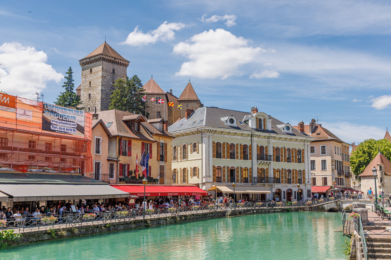 Dieses Bild zeigt das historische Zentrum von Annecy, oft als "Venedig der Alpen" bezeichnet. Im Hintergrund thronen die mittelalterliche Burg Ch&acirc;teau d'Annecy sowie das Palais de l'Isle. Die malerischen, von Restaurants ges&auml;umten Kan&auml;le werden vom kristallklaren Fluss Thiou durchzogen