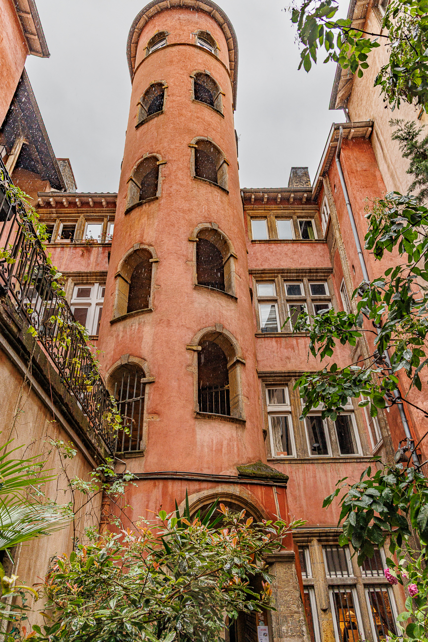 Das Bild zeigt den ber&uuml;hmten rosa Treppenturm des Maison du Crible in der Altstadt von Lyon. Dieses historische Geb&auml;ude aus dem 16. Jahrhundert befindet sich in der Rue du B&oelig;uf und ist f&uuml;r seine markante ockerfarbene Fassade bekannt. Der Turm ist ein zentrales Element einer der bekannten Traboules (versteckte Durchg&auml;nge) im Viertel Vieux Lyon.